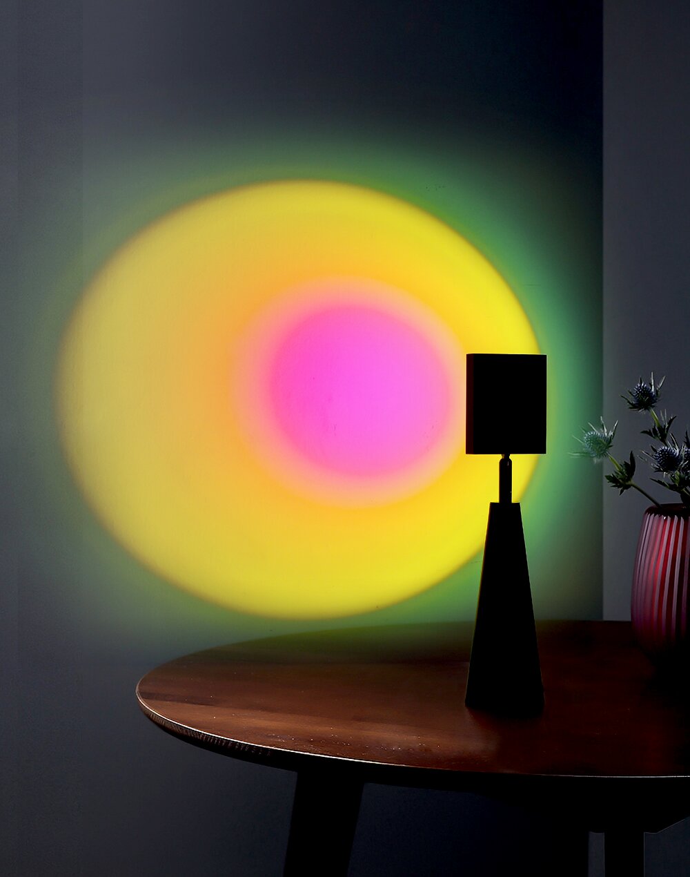 Tischleuchte Ryusei auf einem Tisch, die bunte Lichteffekte an die Wand projiziert. Perspektive von der Seite.