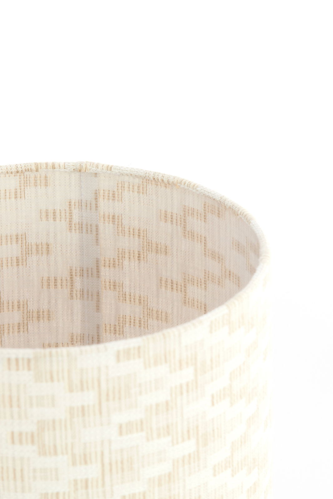 Nahaufnahme eines cremefarbenen Lampenschirms mit feinem, geometrischem Muster, von oben betrachtet.