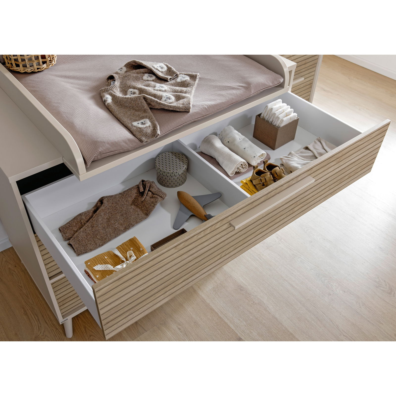 Offene Schublade einer breiten Kommode mit Kinderkleidung und Accessoires, von oben fotografiert.