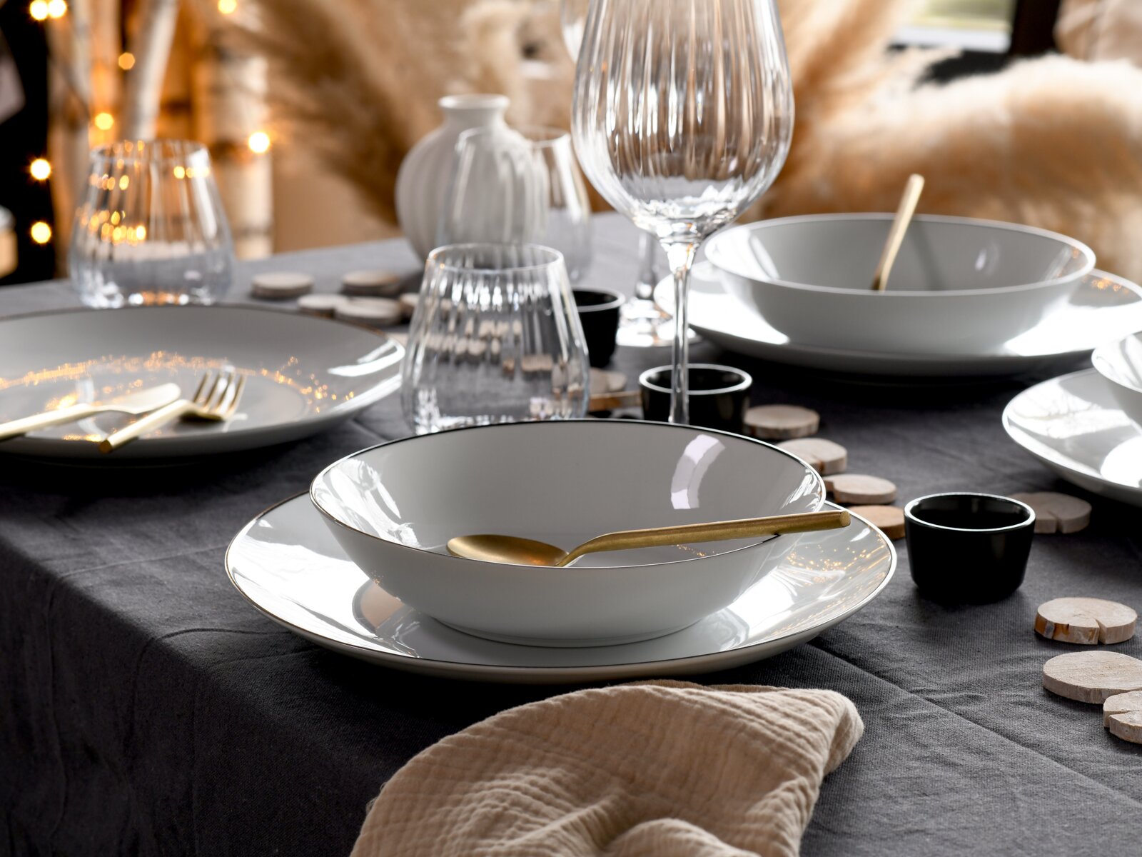 Elegantes Tellerset 18-tlg auf einem festlich gedeckten Tisch mit goldfarbenem Besteck und Gläsern, seitliche Perspektive