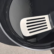 Nahaufnahme eines glänzenden schwarzen Woks mit einem silbernen Pfannenwender, von oben betrachtet.