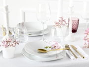 Elegantes weißes Tafelservice mit Orchideen-Motiv, goldfarbenem Besteck, Weingläsern und Kerzenständern auf festlich gedecktem Tisch, Perspektive: leicht erhöhte Frontansicht