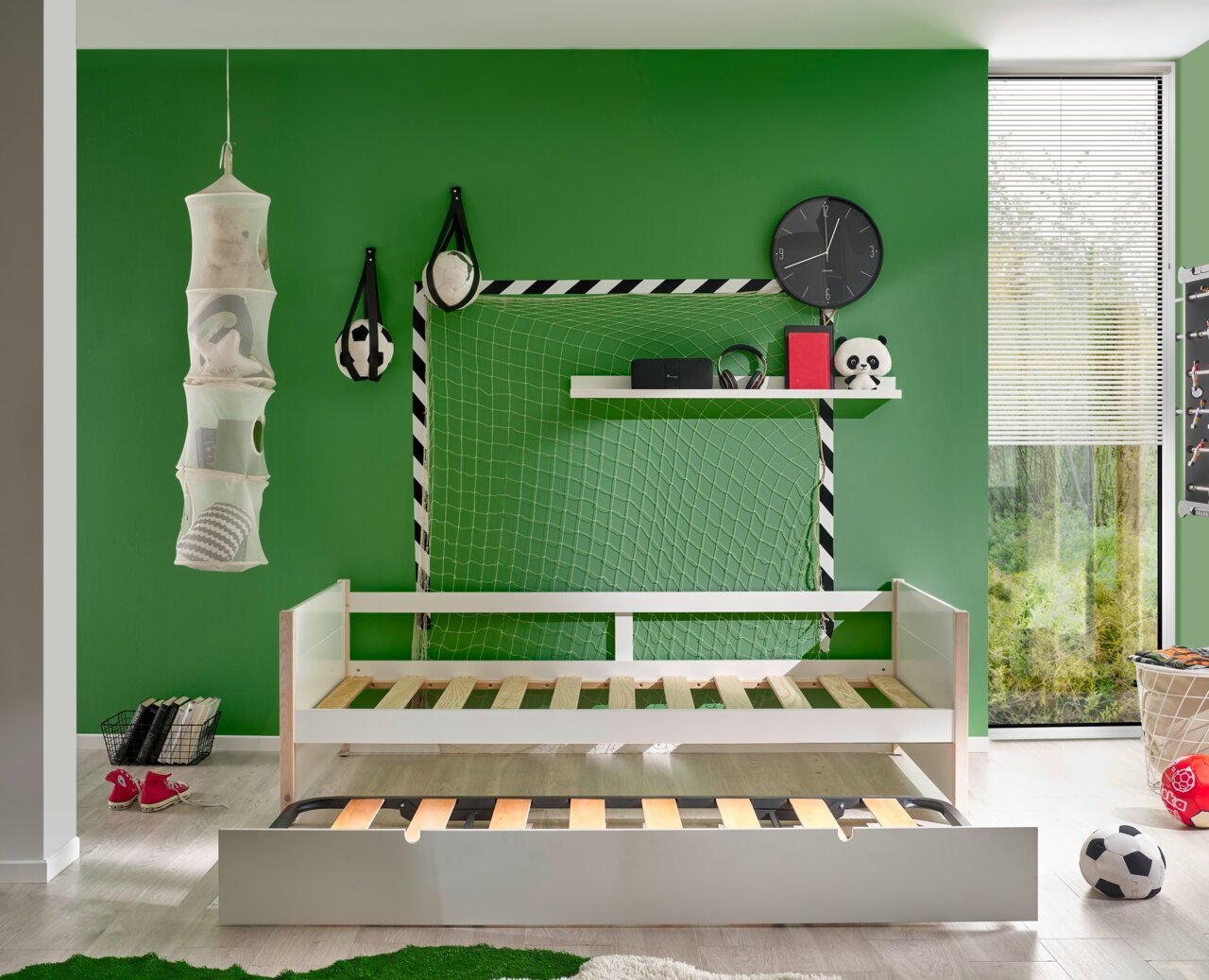Jugendbett mit ausziehbarem Bettkasten, vor grünem Hintergrund mit Fußball-Dekorationen, aus der Frontalperspektive.