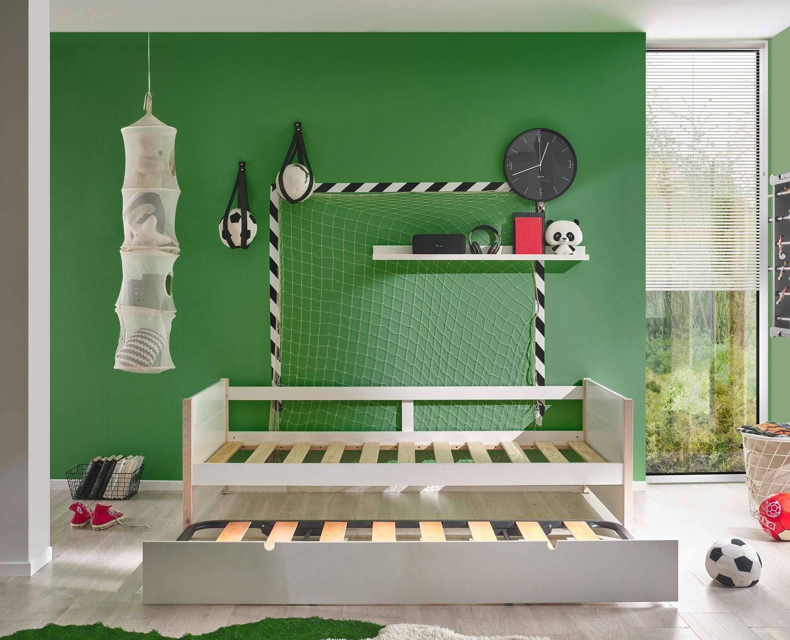 Jugendbett mit ausziehbarem Bettkasten, vor grünem Hintergrund mit Fußball-Dekorationen, aus der Frontalperspektive.