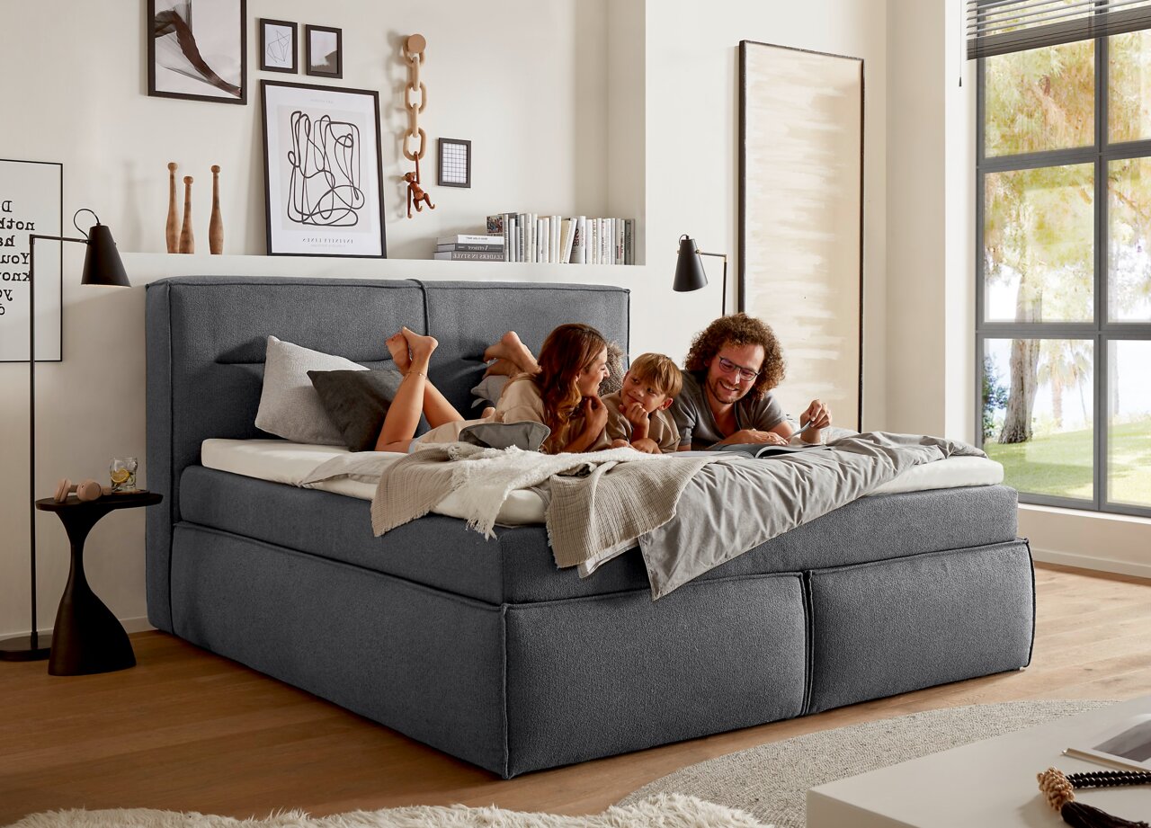 Gemütliches Boxspringbett in einem modernen Schlafzimmer, seitliche Perspektive, mit einer Familie, die darauf entspannt.