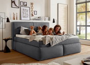 Gemütliches Boxspringbett in einem modernen Schlafzimmer, seitliche Perspektive, mit einer Familie, die darauf entspannt.