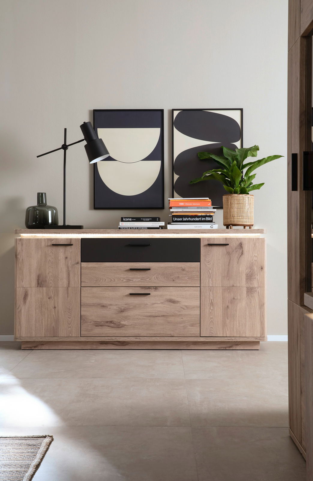 Frontale Ansicht eines modernen Sideboards aus Holz mit schwarzen Akzenten, dekoriert mit Büchern, einer Lampe und einer Pflanze.