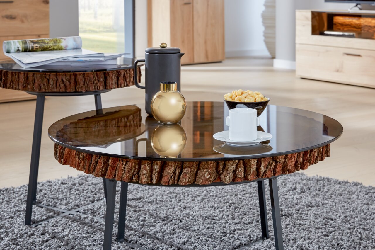 Valnatura Salontafel Runder Couchtisch mit Glasplatte und rustikalem Holzrand, seitliche Perspektive, dekoriert mit einer Tasse, einer goldenen Vase und Snacks.