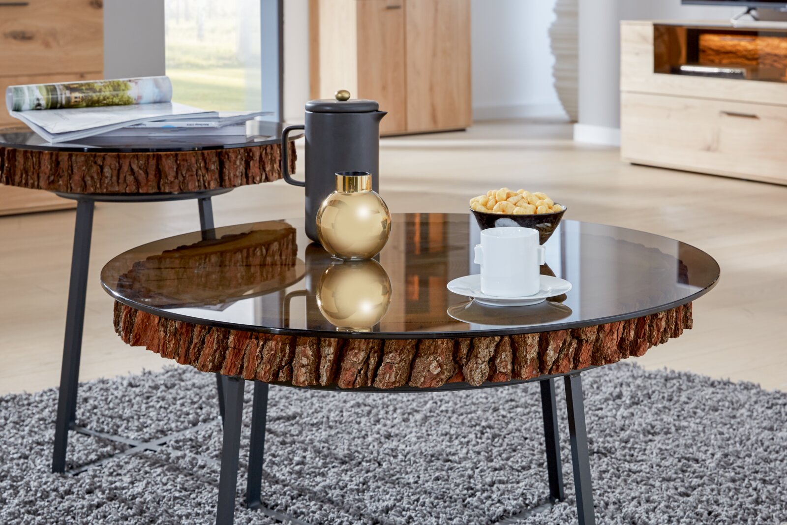 Ronde salontafel met glazen blad en een rustieke houten rand, gezien vanaf de zijkant, versierd met een kopje, een gouden vaas en wat hapjes.