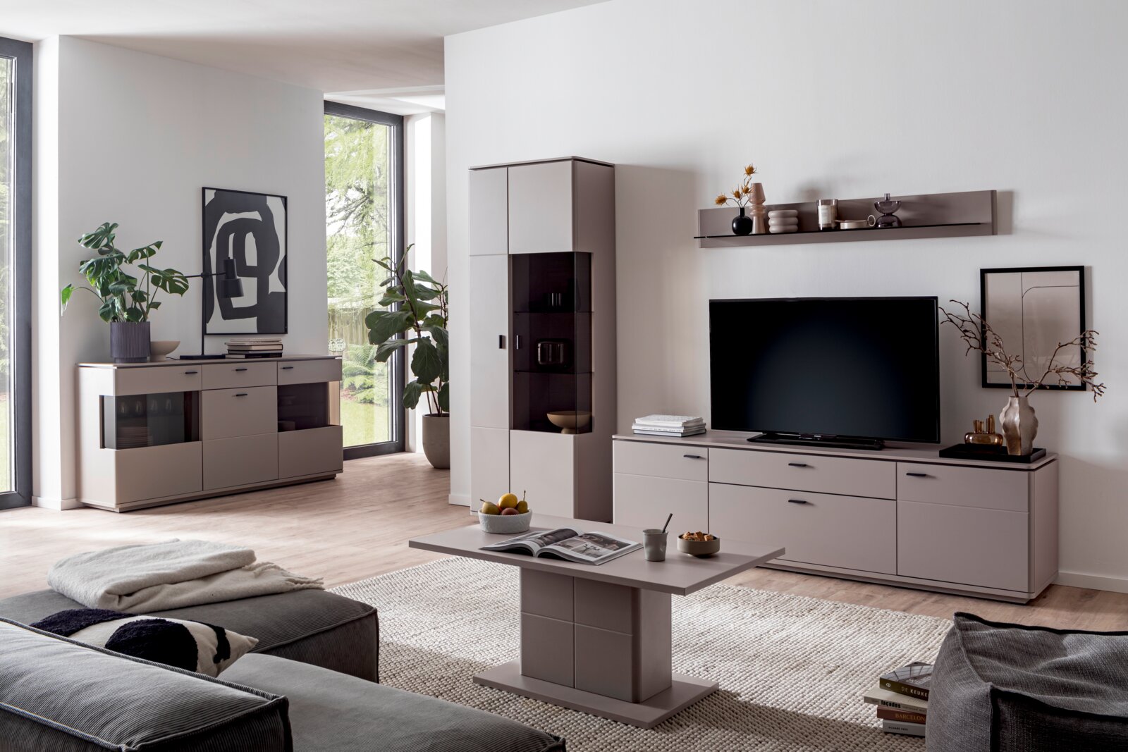 Moderne woonkamer met een lichtgrijze wandmeubel (tv-kast, vitrinekast en dressoir) en bijpassende salontafel, van voren gefotografeerd in een licht schuin perspectief vanaf de linkerkant