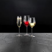 Drei Stielgläser mit Sekt, Rotwein und Weißwein auf einer dunklen Oberfläche, seitliche Perspektive.