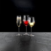 Drei Stielgläser mit Sekt, Rotwein und Weißwein auf einer dunklen Oberfläche, seitliche Perspektive.
