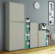 Modulares, hellgraues Büro-Aufbewahrungssystem mit Schranktüren und offenen Fächern mit Aktenordnern, aufgenommen in frontaler Perspektive mit leichtem Blick von rechts in einem modernen Raum.