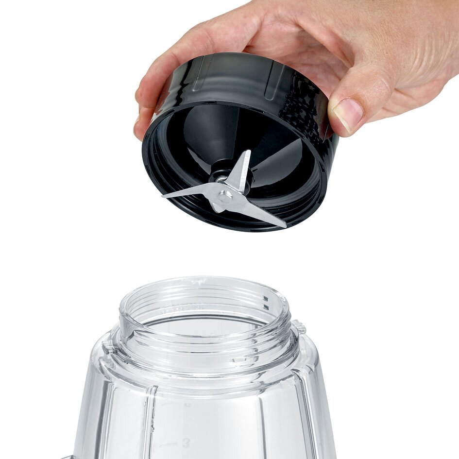 Close-up van een zwarte blender-/smoothiemaker-mesunit met drie metalen messen die boven een transparante beker wordt gehouden, schuin van bovenaf gezien.