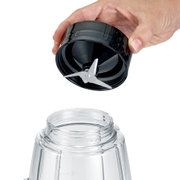 Close-up van een zwarte blender-/smoothiemaker-mesunit met drie metalen messen die boven een transparante beker wordt gehouden, schuin van bovenaf gezien.