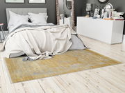 Designer Teppich in einem modernen Schlafzimmer, Perspektive von der Seite des Bettes, mit einem eleganten, gelb-grauen Muster auf hellem Holzboden.