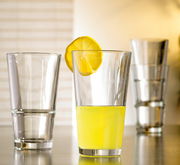 Trinkglas Event 330ml, gefüllt mit gelbem Getränk und Zitronenscheibe am Rand, im Vordergrund, mit weiteren leeren Gläsern im Hintergrund.