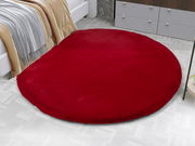 Runder roter Fellteppich auf einem hellen Boden, neben einem Bett und einer Kommode, aus der Vogelperspektive.