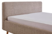 Seitliche Ansicht eines Polsterbettgestells mit beigem Stoffbezug und Holzfüßen.
