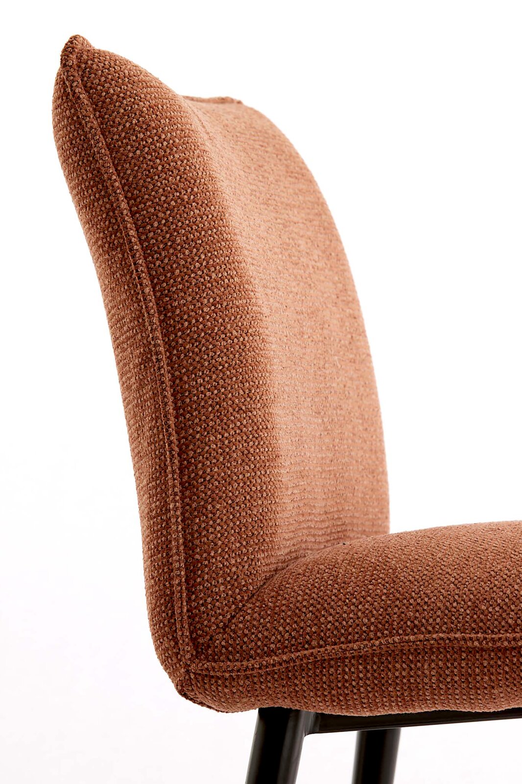 Close-up van een gestoffeerde stoel met een bruine, gestructureerde stoffen bekleding en een zwart metalen frame, gezien vanaf de zijkant (licht van achteren) tegen een witte achtergrond.