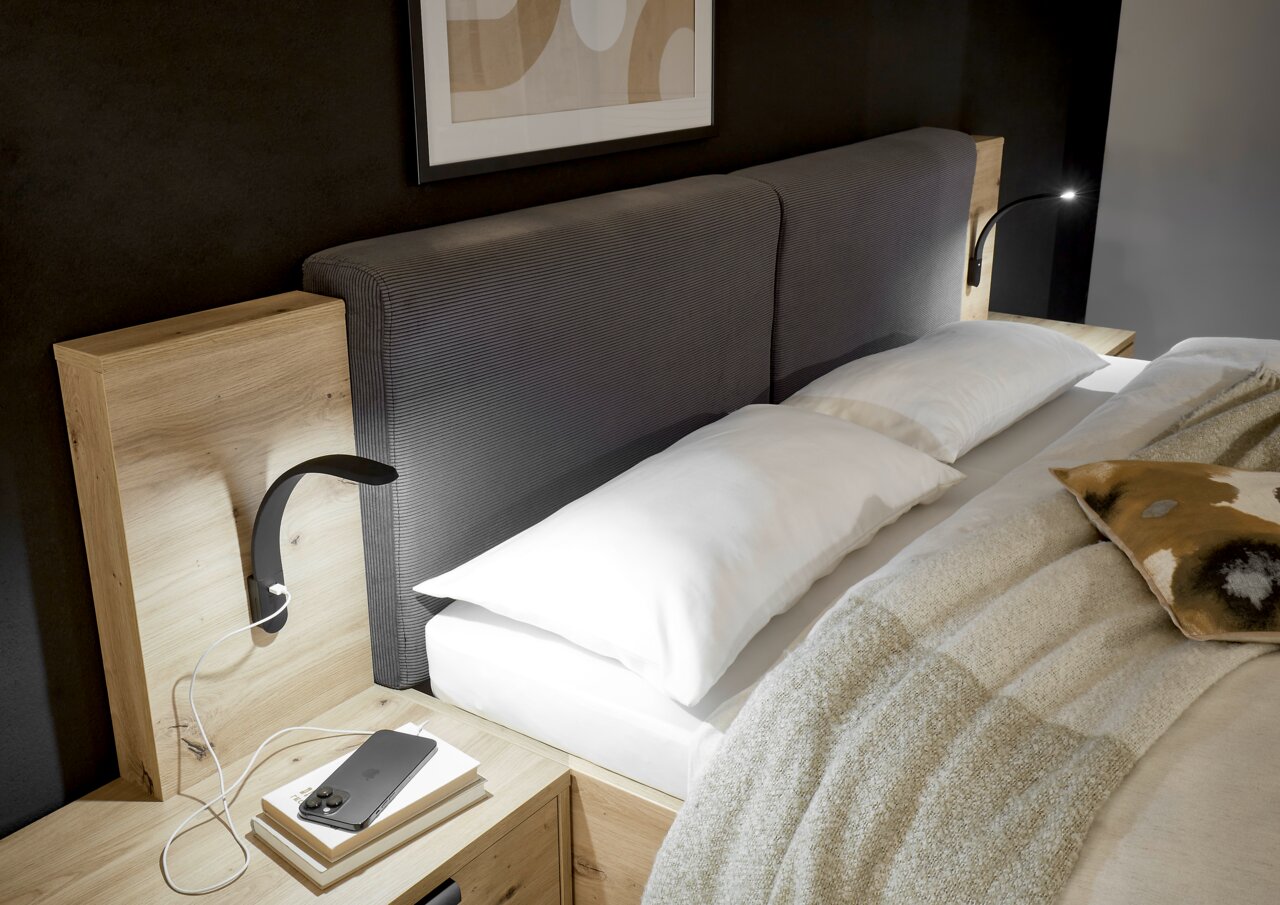 Leseleuchte Silka 2er-Set in einem modernen Schlafzimmer, montiert an einem Holzkopfteil mit grauem Polster, seitliche Perspektive.