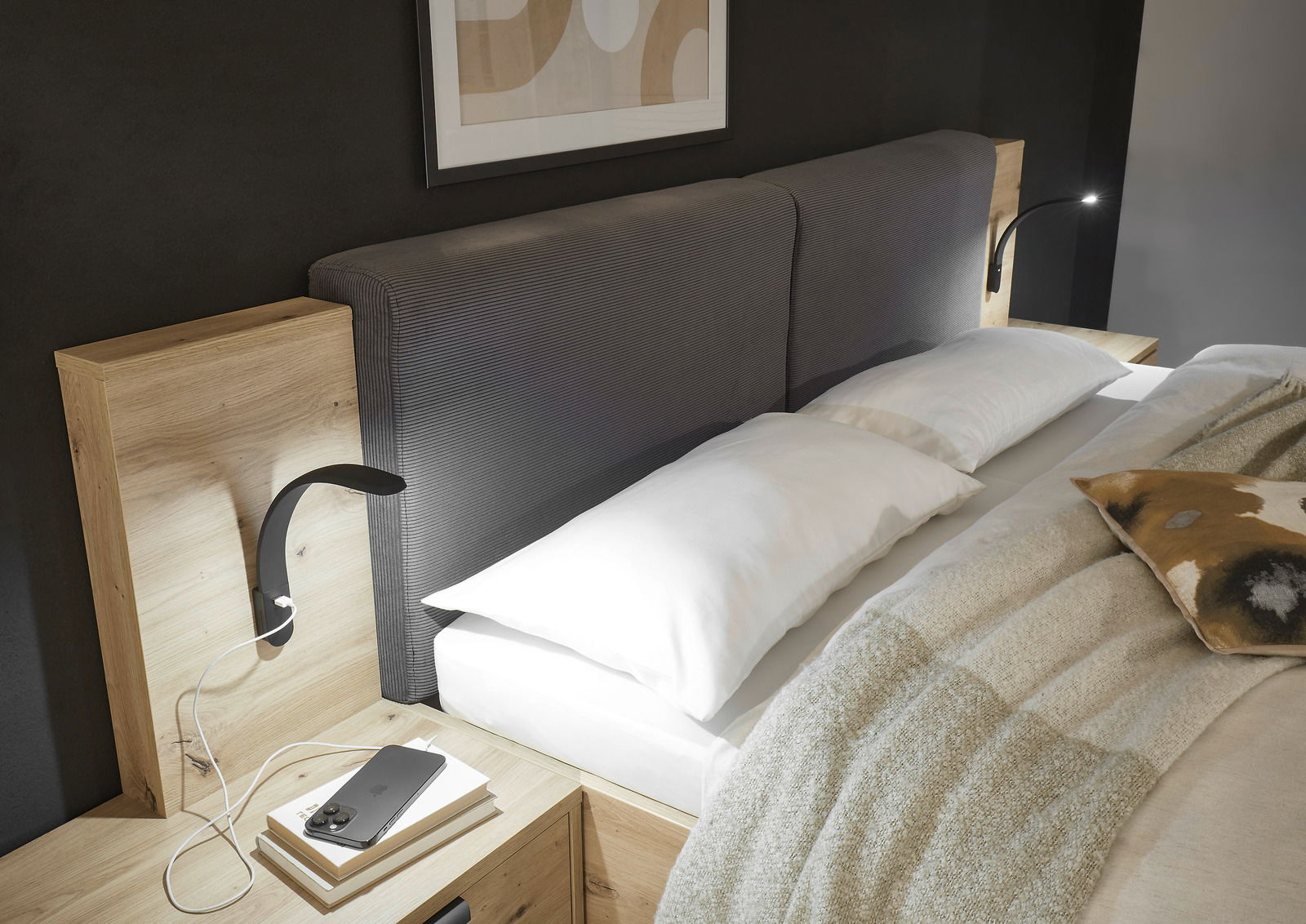 Leseleuchte Silka 2er-Set in einem modernen Schlafzimmer, montiert an einem Holzkopfteil mit grauem Polster, seitliche Perspektive.