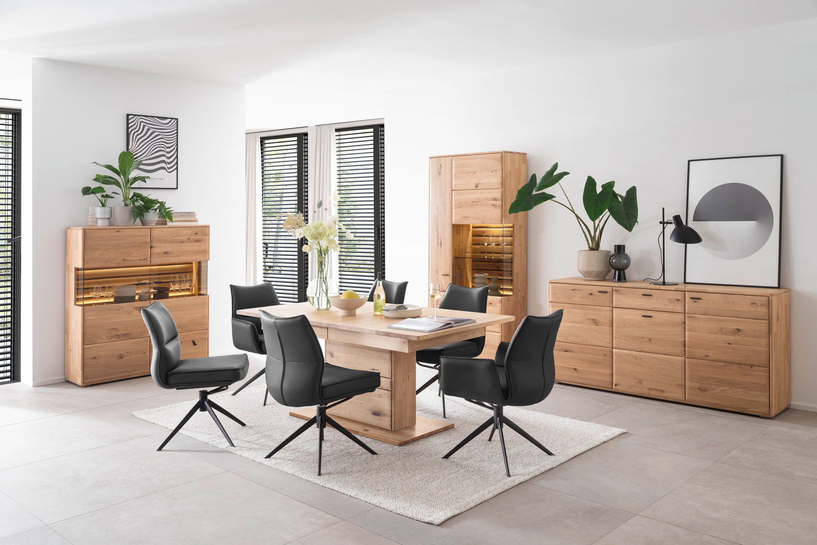 Esszimmer mit modernen schwarzen Stühlen und einem Holztisch, umgeben von Holzmöbeln und Pflanzen, aus einer seitlichen Perspektive.