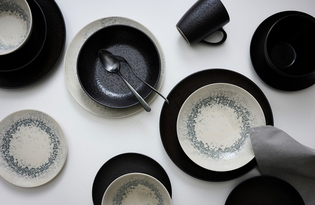 Vogelperspektive auf ein 18-teiliges Geschirrset in Graphitfarbe mit modernen, gesprenkelten Mustern, bestehend aus Tellern, Schalen und Tassen.