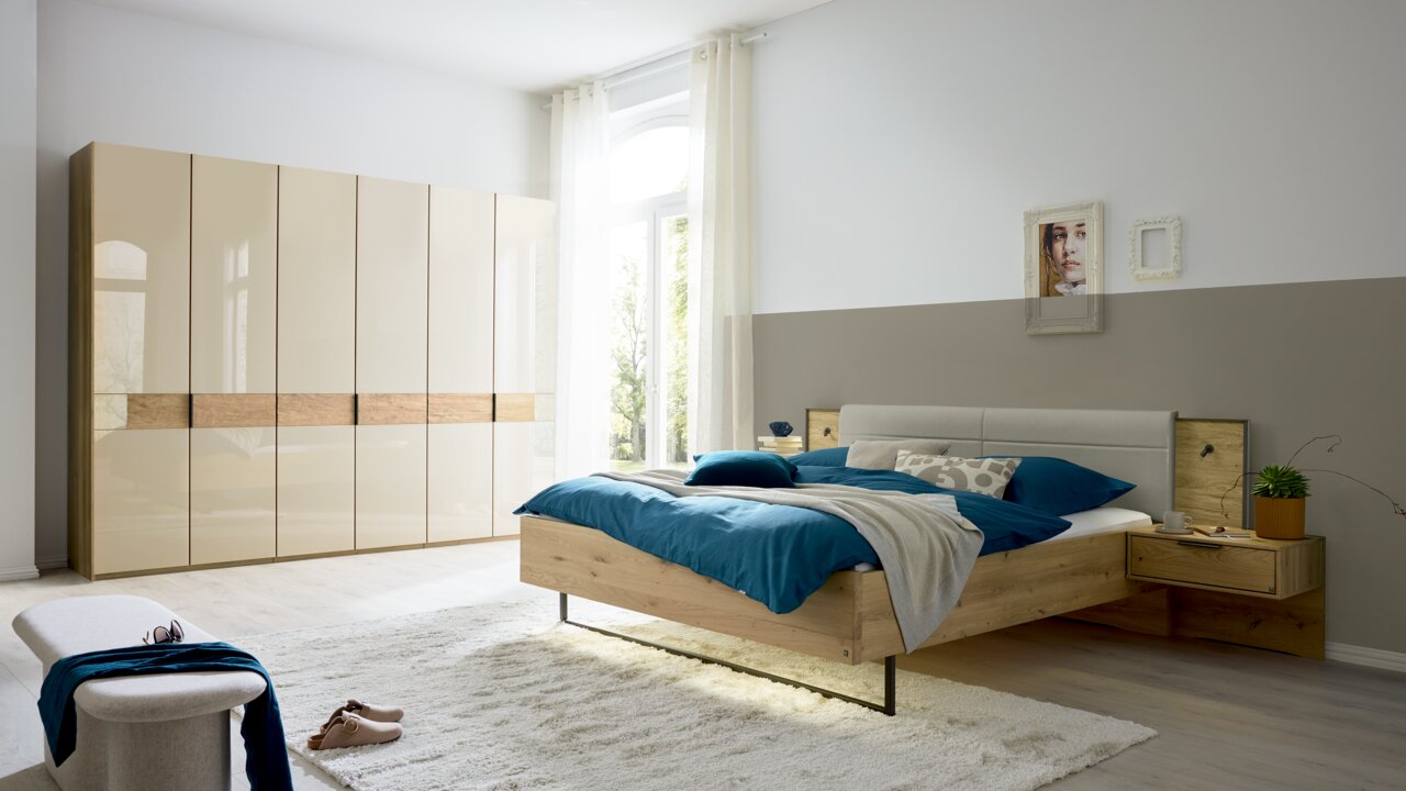 Modernes Schlafzimmer mit einem großen Kleiderschrank und einem gemütlichen Bett in Holzoptik, seitliche Perspektive.