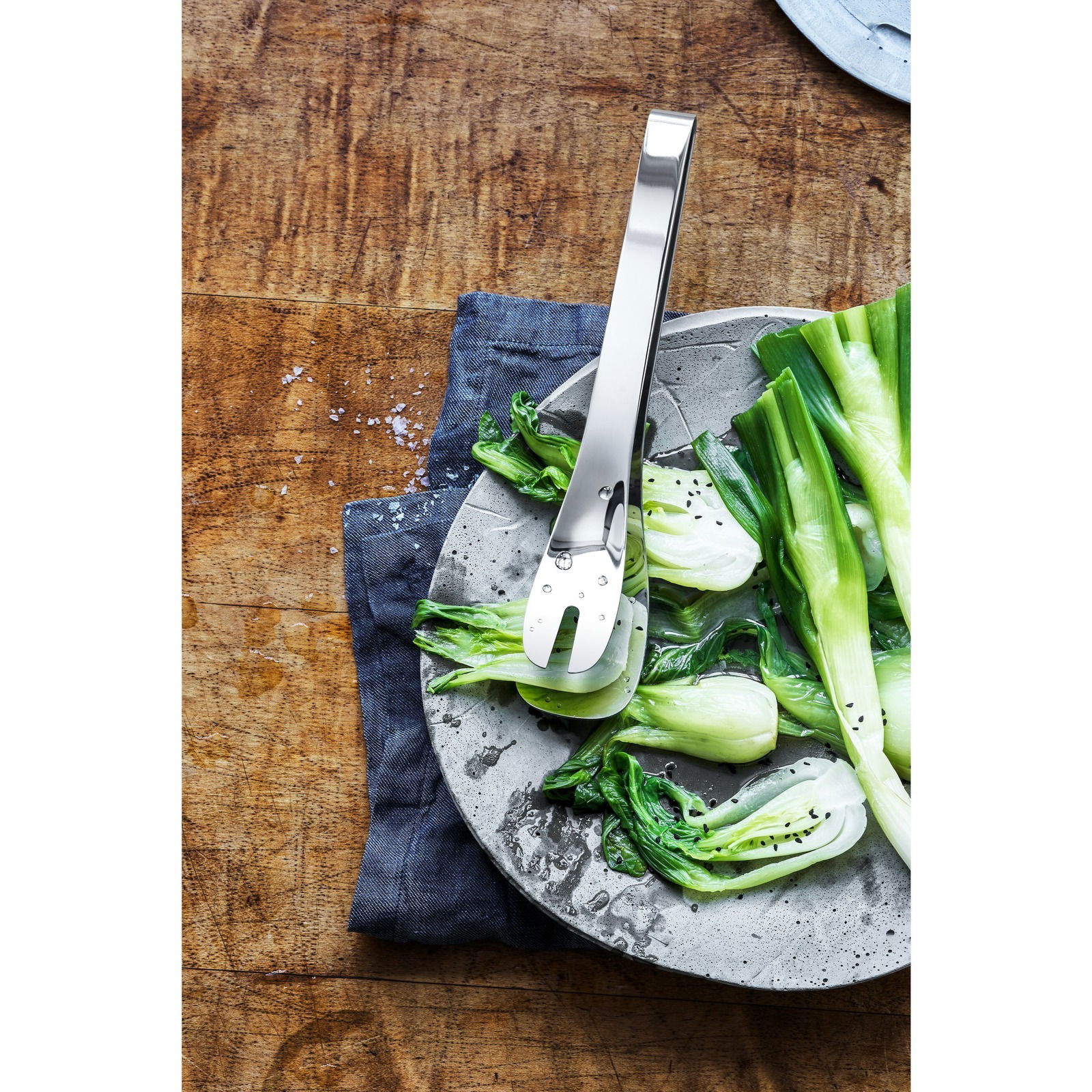 Universalzange NUOVA aus Edelstahl, auf einem Teller mit frischem Gemüse, von oben fotografiert.