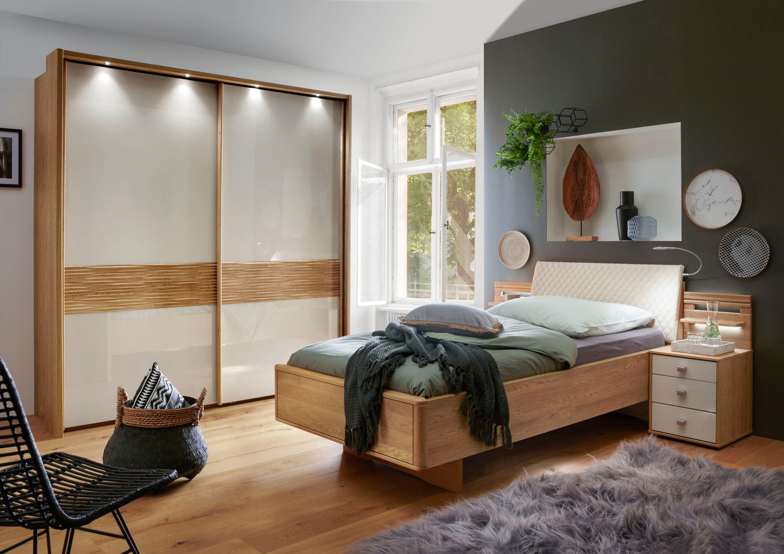 Nachtschrank aus Holz mit drei Schubladen, neben einem modernen Bett in einem stilvoll eingerichteten Schlafzimmer, seitliche Perspektive.