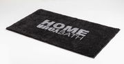 Grauer Badteppich mit der Aufschrift 'HOME BATH', perspektivisch von der Seite fotografiert.