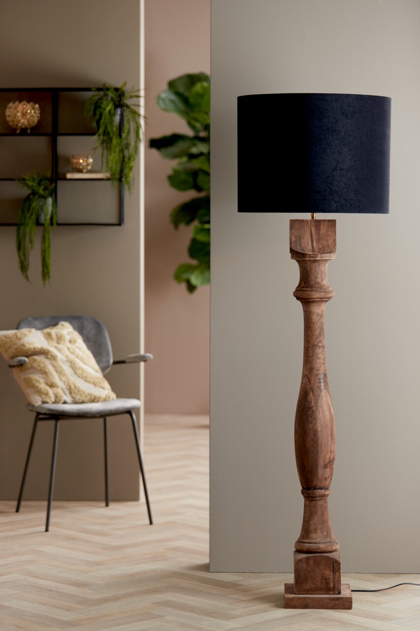 Stehlampe mit einem zylindrischen, schwarzen Lampenschirm und einem kunstvoll geschnitzten Holzfuß, seitliche Perspektive.