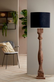 Stehlampe mit einem zylindrischen, schwarzen Lampenschirm und einem kunstvoll geschnitzten Holzfuß, seitliche Perspektive.