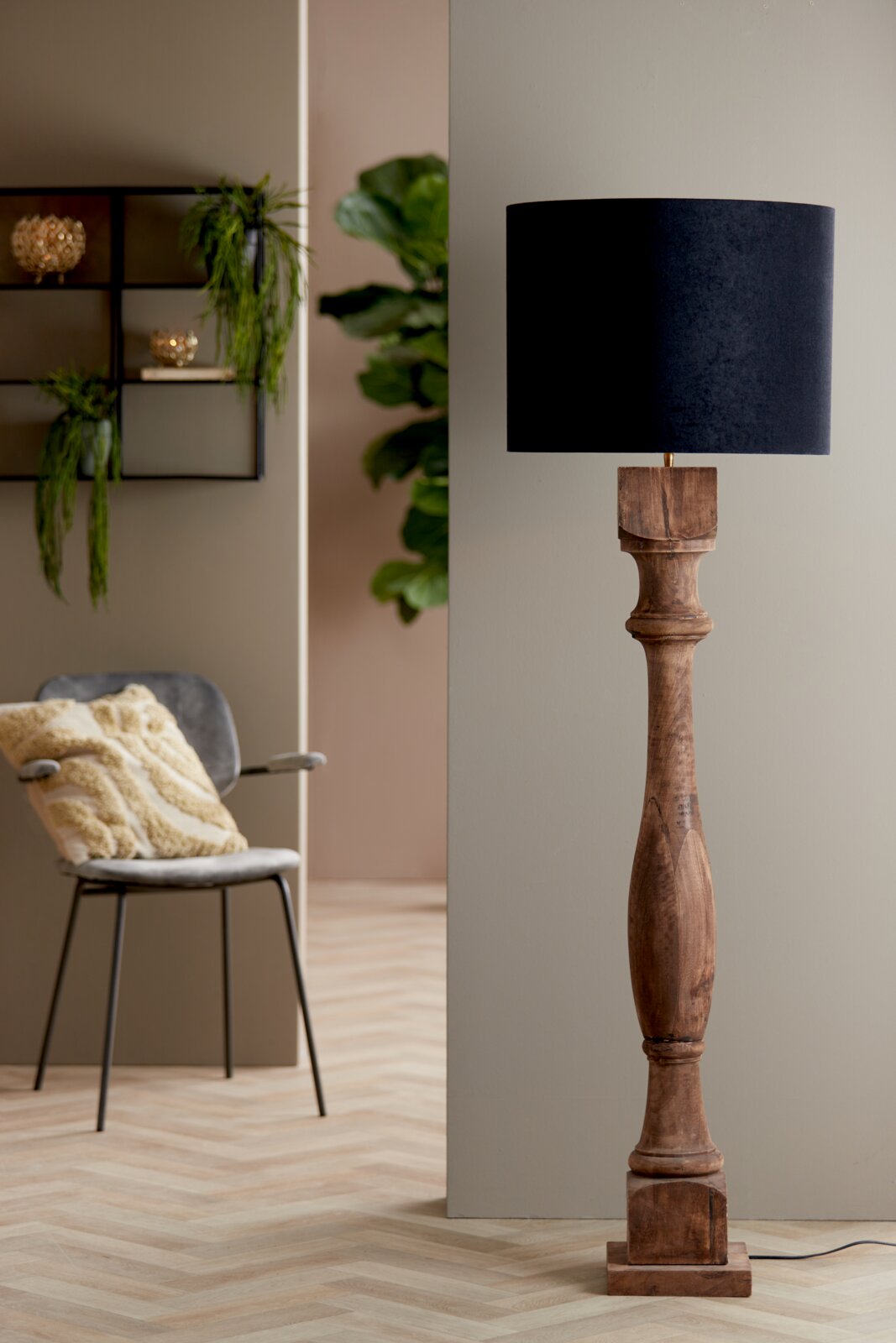 Stehlampe mit einem zylindrischen, schwarzen Lampenschirm und einem kunstvoll geschnitzten Holzfuß, seitliche Perspektive.