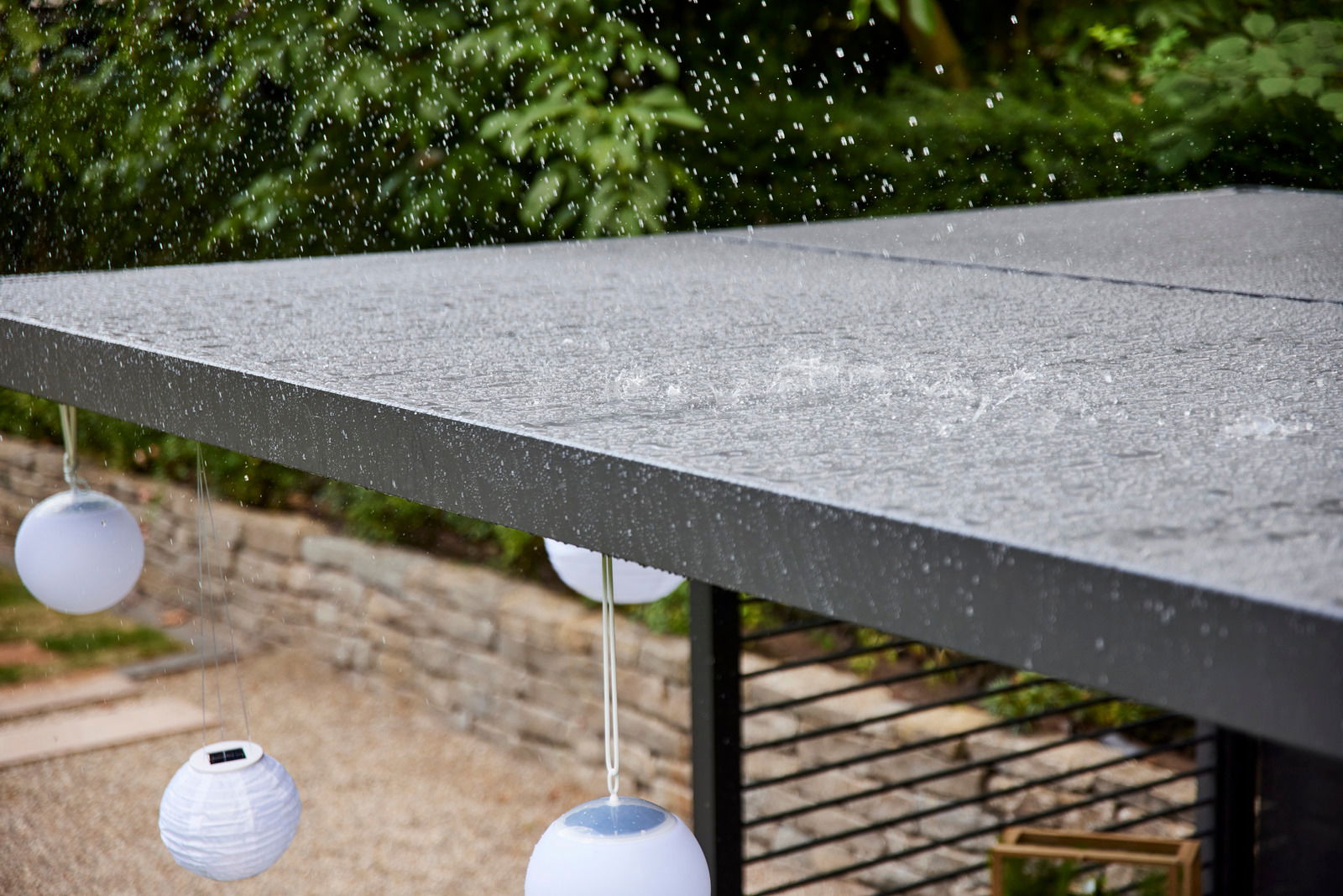 Regentropfen fallen auf ein modernes, flaches Dach mit hängenden weißen Laternen, seitliche Perspektive.
