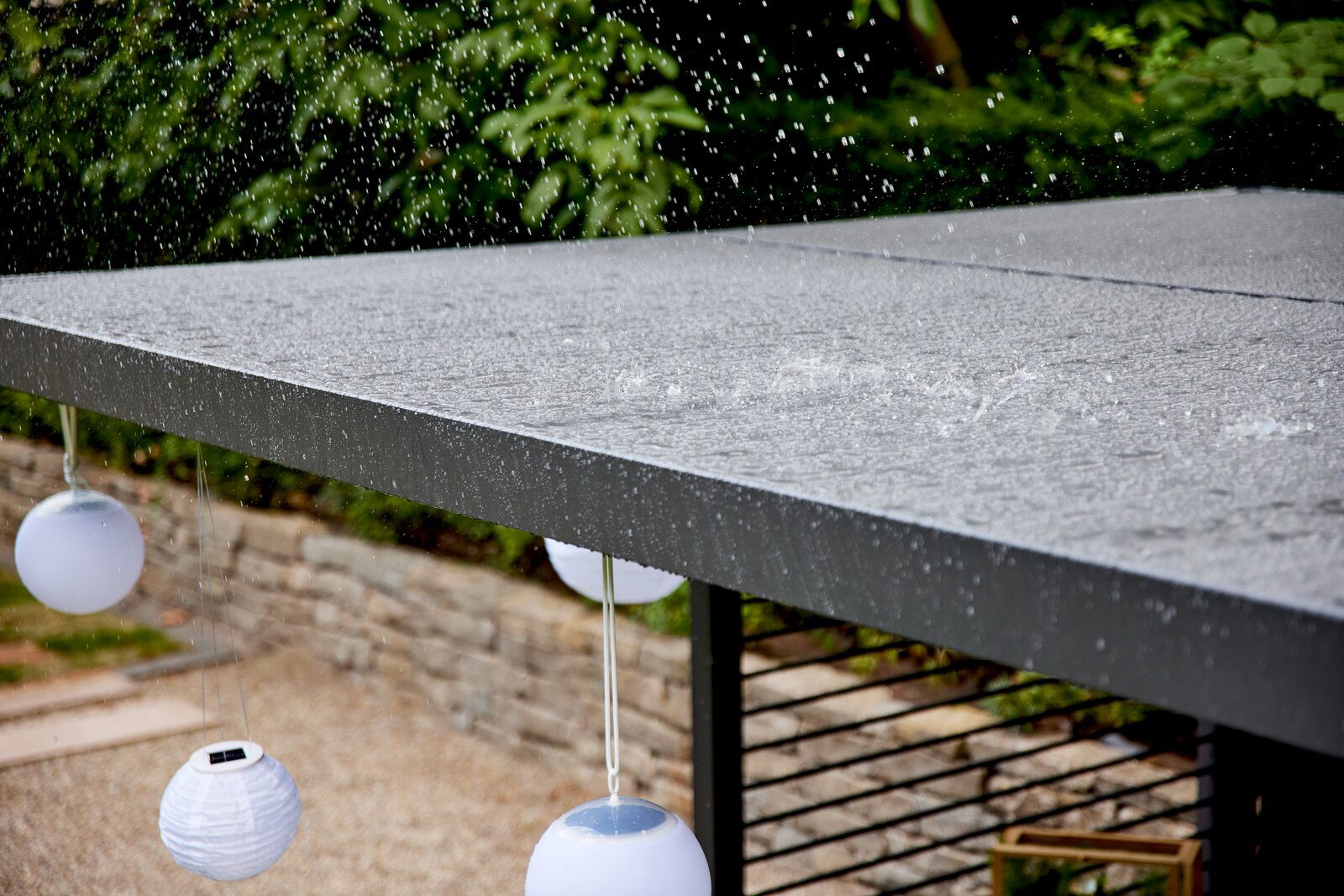 Siena Garden Pergola Basis Erweiter. VIVERA Regentropfen fallen auf ein modernes, flaches Dach mit hängenden weißen Laternen, seitliche Perspektive.