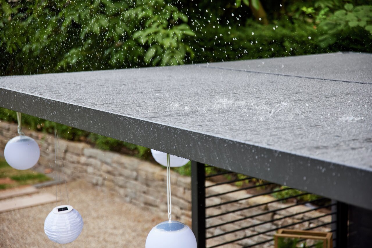 Regentropfen fallen auf ein modernes, flaches Dach mit hängenden weißen Laternen, seitliche Perspektive.