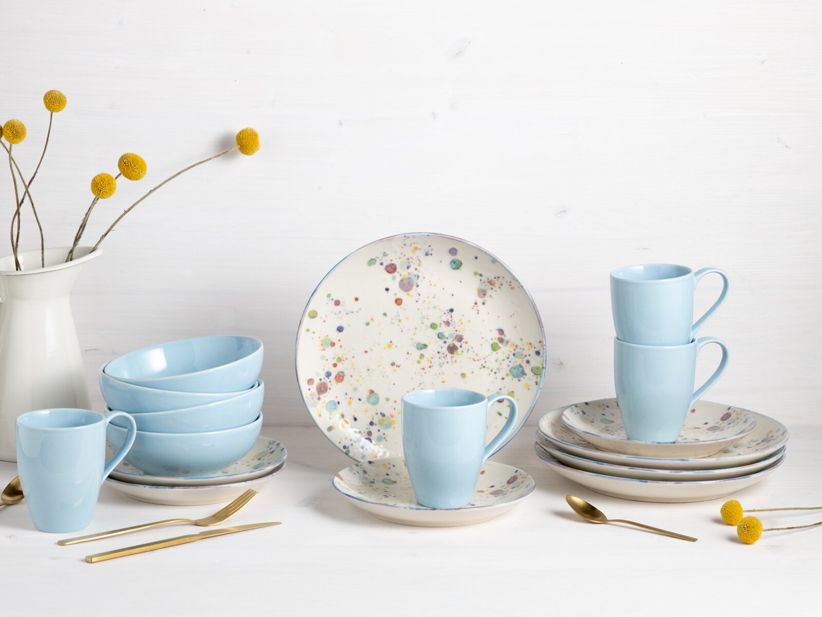 Pastellblaues Geschirr-Set mit Tassen, Schalen und Tellern mit buntem Sprenkelmuster, arrangiert auf weißem Hintergrund, Frontansicht auf Augenhöhe.