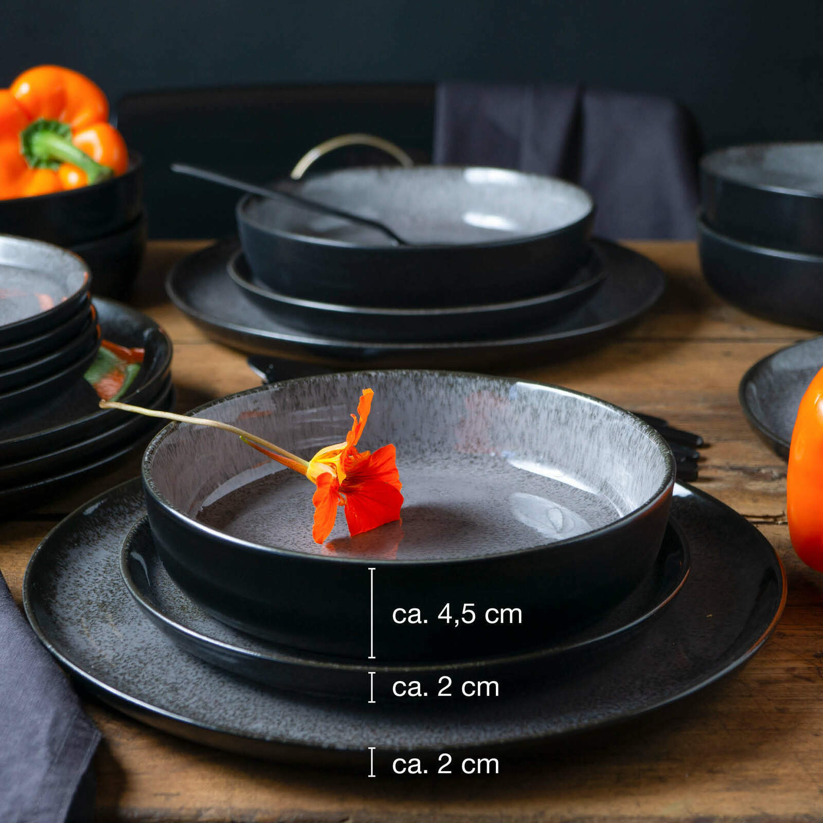 Anthrazitfarbenes 18-teiliges Tafelservice mit modernen, matten Schalen und Tellern, dekoriert mit einer orangefarbenen Blume, seitliche Perspektive