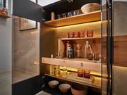 Geöffnete Wandkombination mit beleuchteten Holzregalen, gefüllt mit Gläsern, Flaschen und Schalen, aus der Perspektive von vorne.