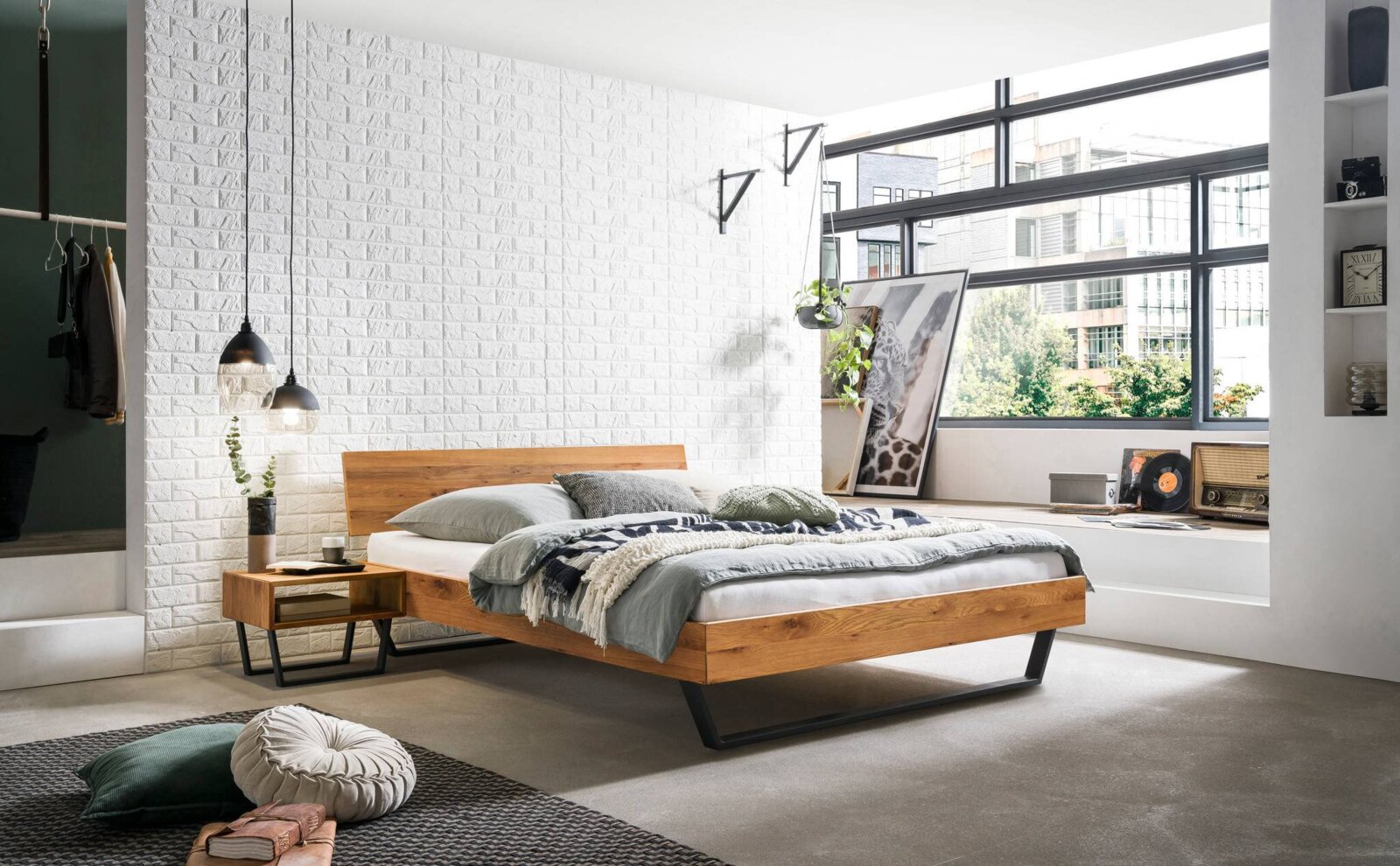 Modernes Bettgestell aus Holz mit schwarzem Metallrahmen, seitliche Perspektive, in einem stilvoll eingerichteten Schlafzimmer mit großen Fenstern und weißen Backsteinwänden.