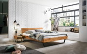 Modernes Bettgestell aus Holz mit schwarzem Metallrahmen, seitliche Perspektive, in einem stilvoll eingerichteten Schlafzimmer mit großen Fenstern und weißen Backsteinwänden.