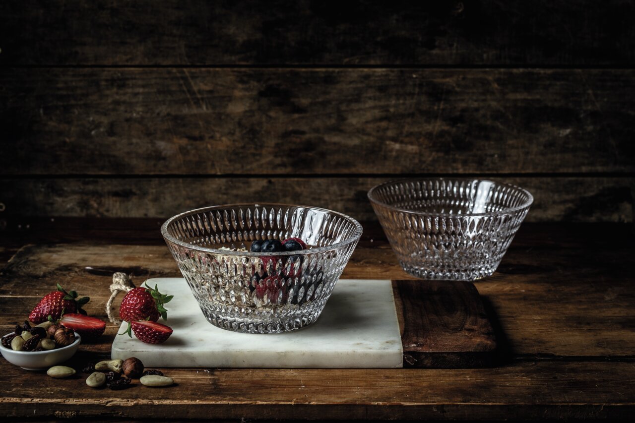 Zwei durchsichtige Glasschalen mit Ethno-Muster, eine gefüllt mit Beeren und Nüssen, auf einem rustikalen Holztisch von schräg oben fotografiert.