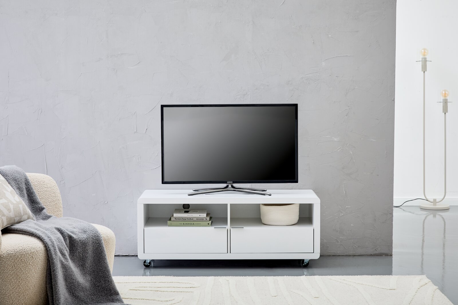 XORA TV-Lowboard LIMA Weißes TV-Lowboard mit zwei offenen Fächern und zwei Schubladen, darauf steht ein Flachbildfernseher, frontal fotografiert.