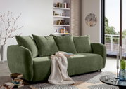 Groene functionele bank in een moderne woonkamer, gezien vanaf de zijkant, versierd met kussens en een deken.