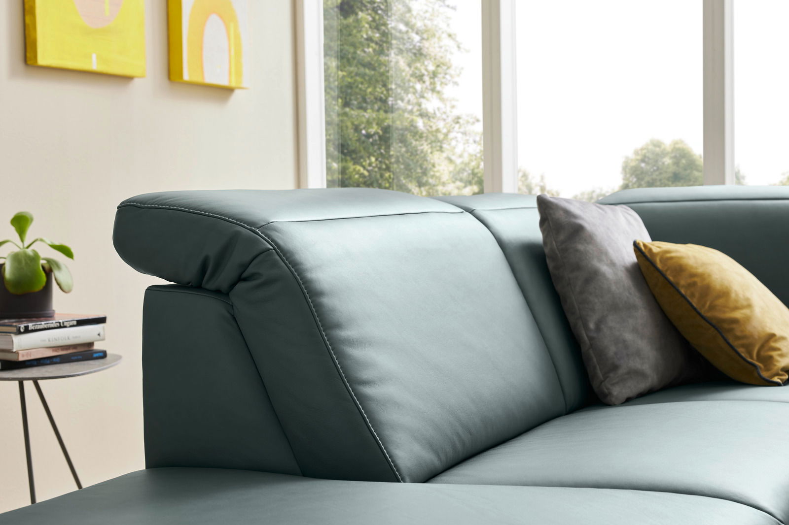 Nahaufnahme einer modernen Eckgarnitur in grünem Leder mit zwei dekorativen Kissen, im Hintergrund ein Fenster mit Blick ins Grüne.