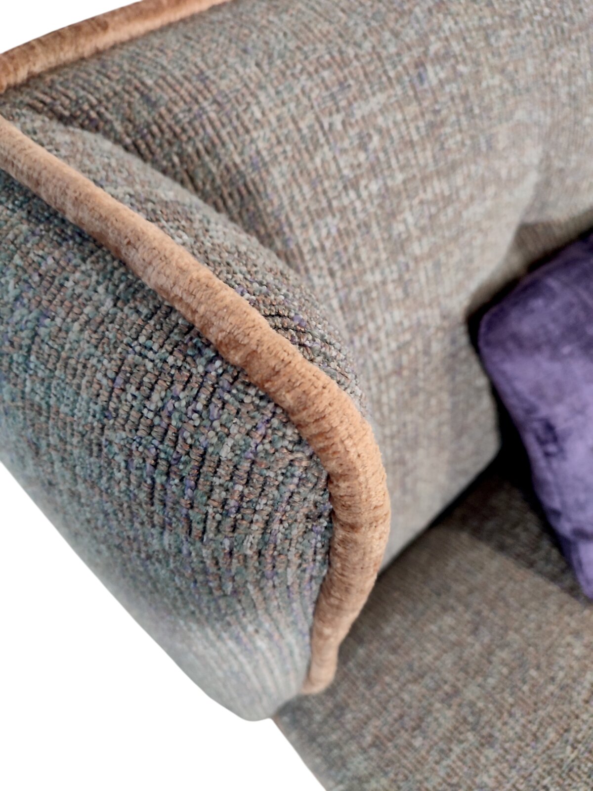 Detailaufnahme einer Sofalehne mit grob gewebtem, meliertem Stoff in Grau-Blau und beigem Keder, schräg von oben fotografiert; rechts ist ein violettes Kissen teilweise sichtbar.