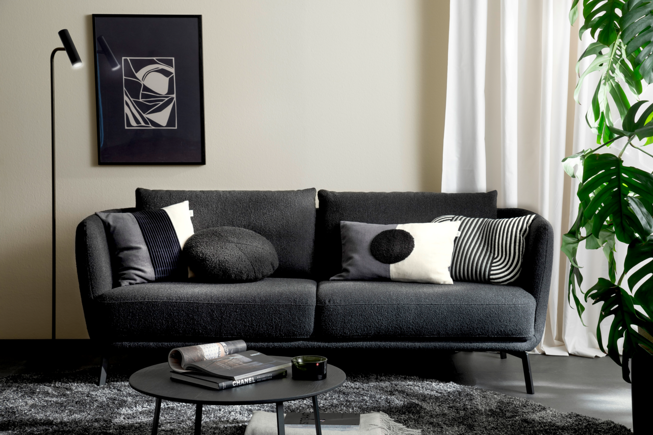 Modernes Wohnzimmer mit einem dunkelgrauen Sofa, dekoriert mit stilvollen Zierkissen in Schwarz-Weiß-Mustern, aus der Perspektive von vorne.