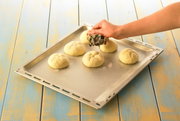 Hand stempelt Brötchen auf einem Backblech mit einem Brötchenstempel, von oben fotografiert.